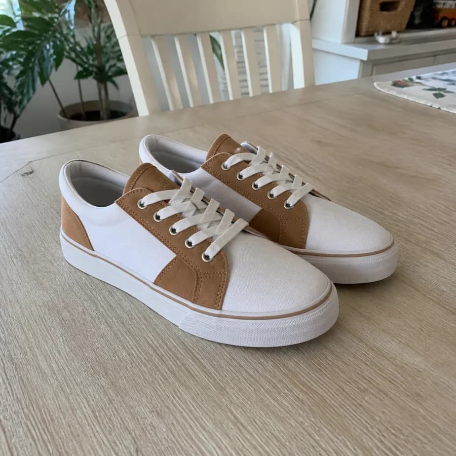 Par de zapatillas blancas y color suela fotografiadas sobre una mesa con muebles domésticos detrás.
