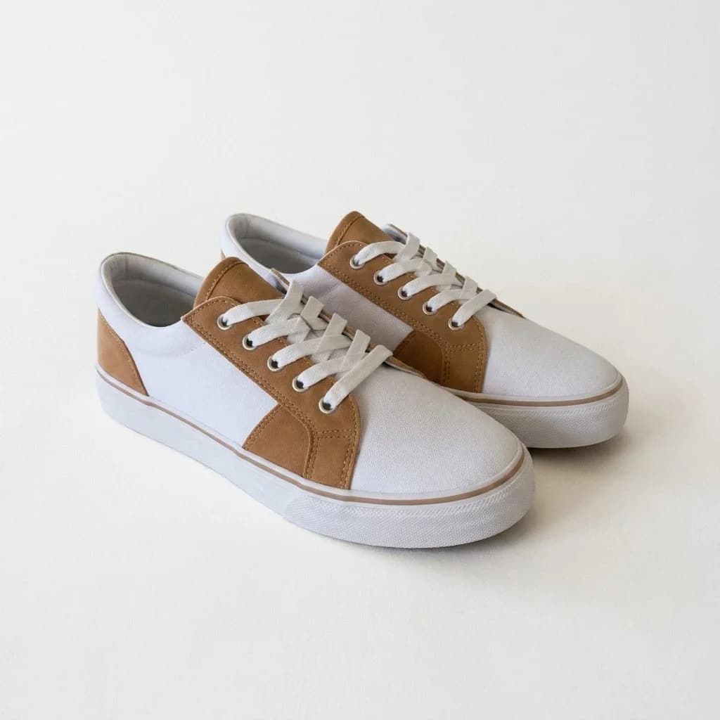 Par de zapatillas blancas y color suela centradas sobre fondo claro continuo con sombra de apoyo suave.