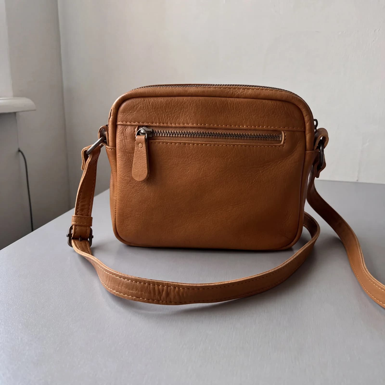 Cartera de cuero color suela mejorada en alta resolución, con textura, cierre y costuras más definidos, sobre el mismo fondo doméstico.