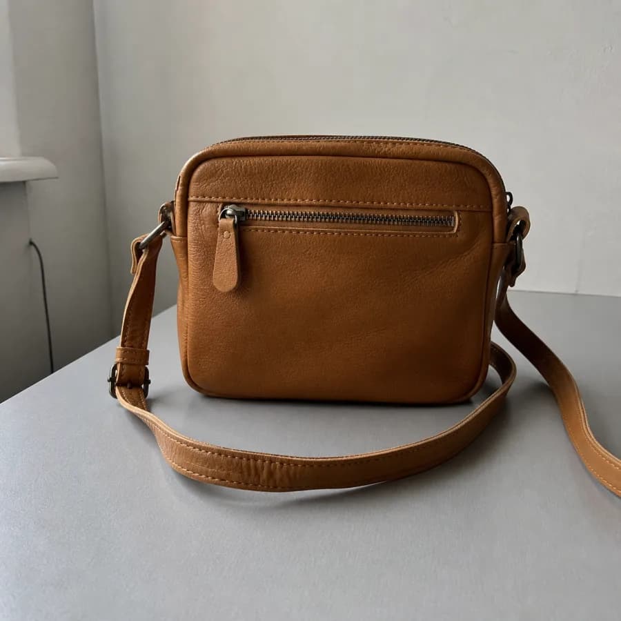 Cartera de cuero color suela fotografiada sobre una mesa, con pared y cable visibles en el fondo.